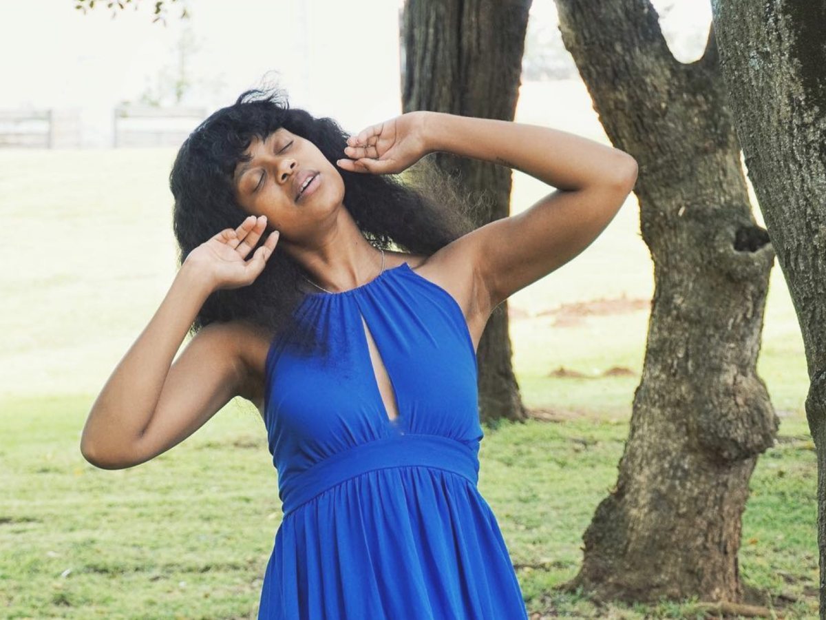 black woman in blue dress with eyes closed and posing